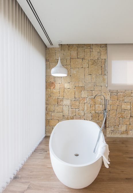 Bañera exenta en dormitorio con pared de piedra en casa de diseño Cumbres | Chiralt Arquitectos Valencia
