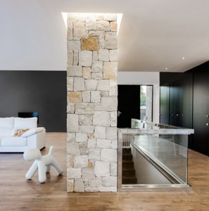Salón y entrada con muro de piedra, con suelo porcelánico efecto madera en casa pasiva | Chiralt Arquitectos Valencia