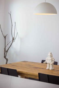 Lámpara de comedor blanca y redonda. Mesa de comedor de madera con sillas negras.Decoración de comedor estilo nórdico con mesa de madera y robot en reforma de casa. Chiralt Arquitectos Valencia.
