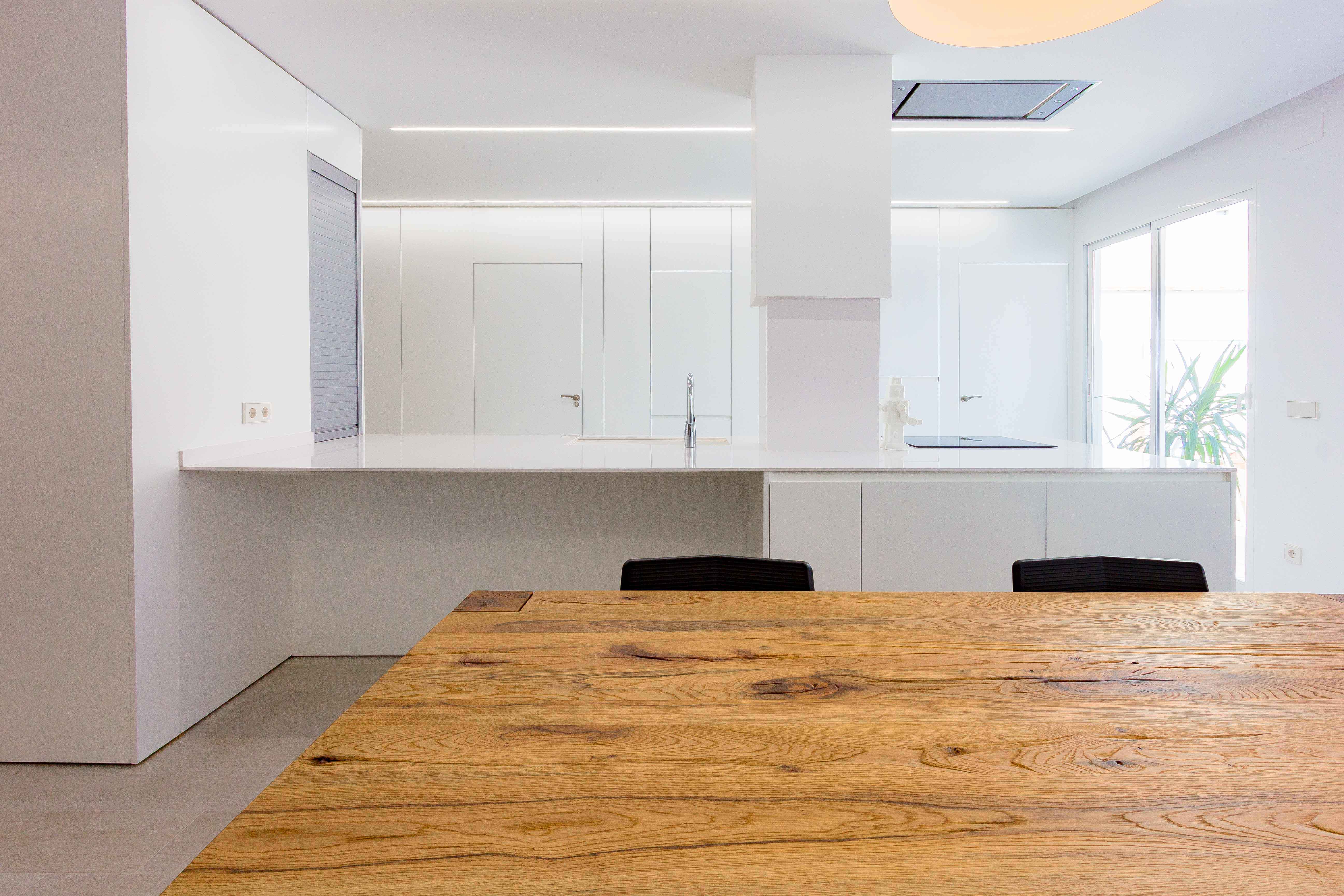 Cocina comedor minimalista con mesa de madera rústica en reforma de casa. Chiralt Arquitectos Valencia.