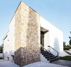 Entrada de casa moderna con pared de piedra y escaleras con barandilla de acero