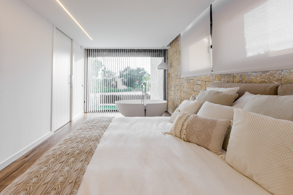 Bañera exenta en dormitorio con vistas al jardin y pared de piedra en casa de diseño Cumbres | Chiralt Arquitectos Valencia