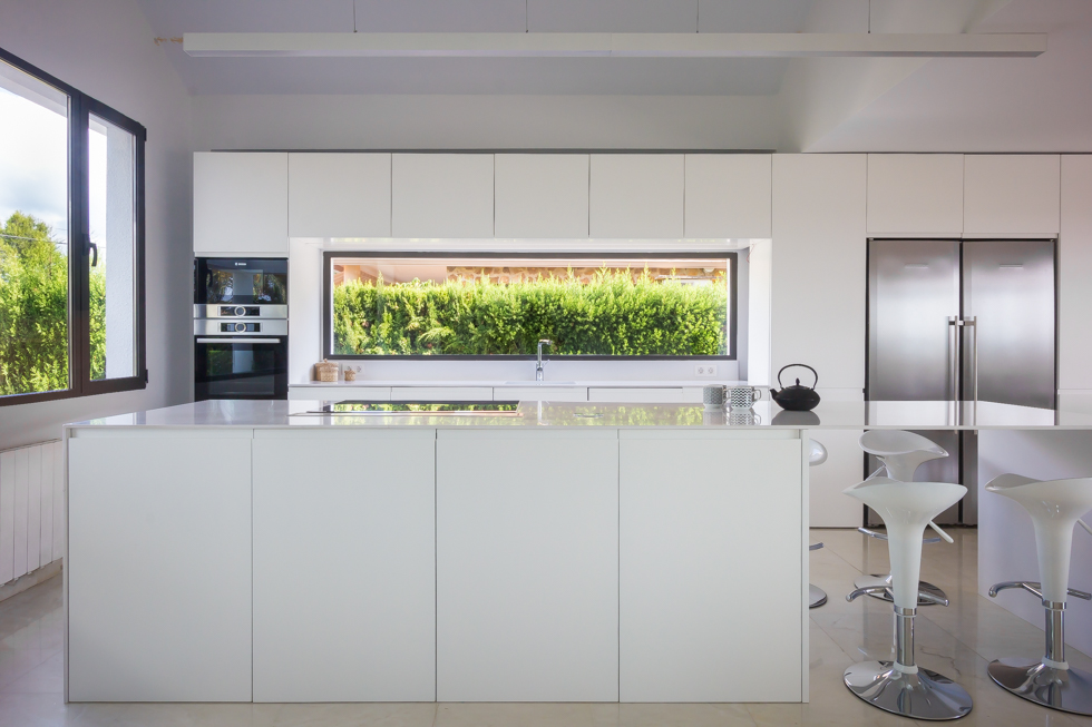 Cocina moderna blanca con isla con ventana en vivienda mediterránea. Chiralt Arquitectos Valencia