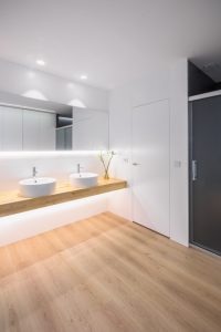 Baño moderno con dos lavabos sobre encimera de madera y suelo parquet en vivienda estilo nórdico - Chiralt Arquitectos Valencia