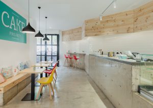 cafetería-de-diseño-en-Valencia-con mostrador de hormigon moderno y minimalista.ladrillos tipo metro y madera. sillas de colores