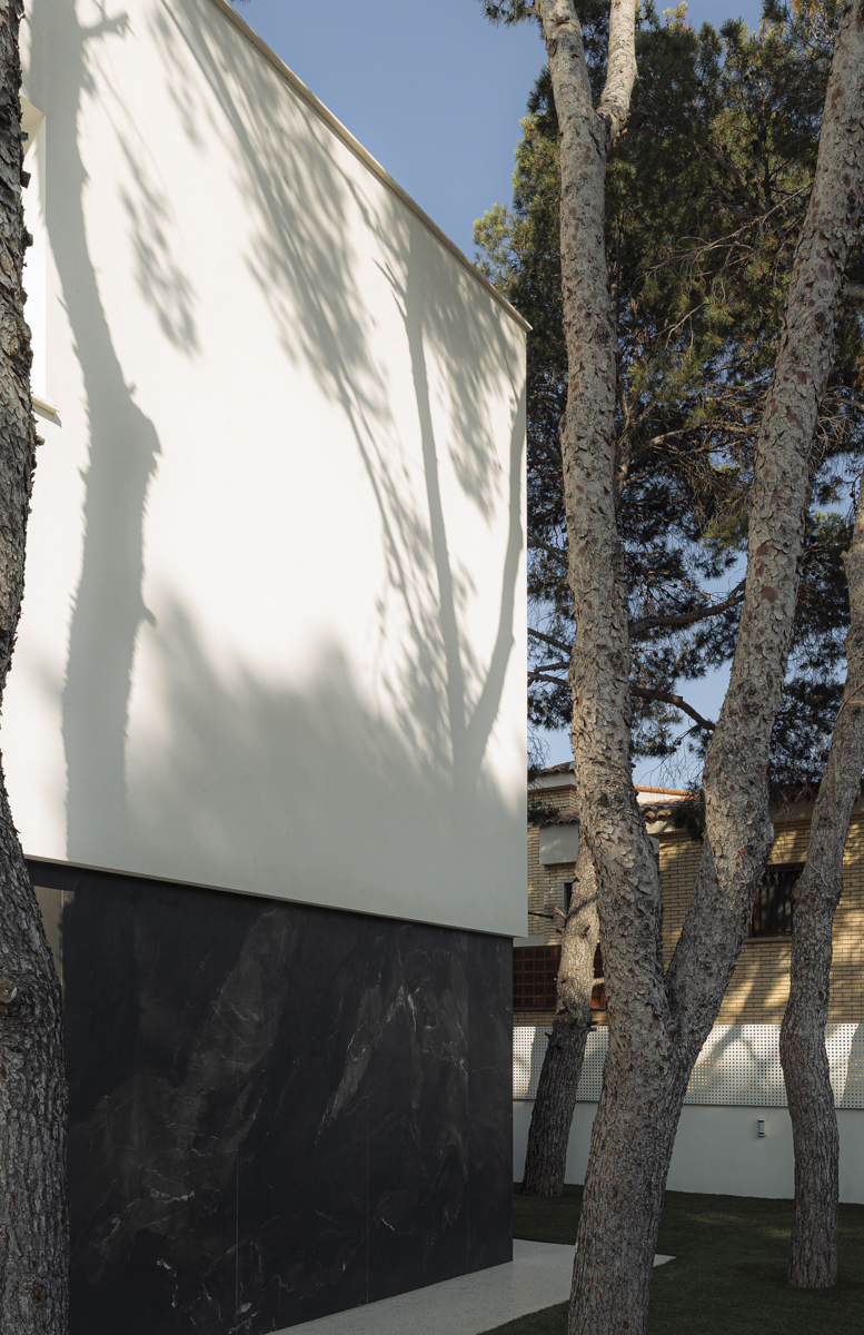 fachada blanca de casa moderna en Valencia con troncos de pinos en primer plano
